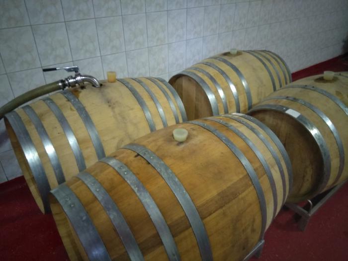 Vier Barriques vor einer Fliesenwand, eines davon wird über einen Schlauch befüllt.
